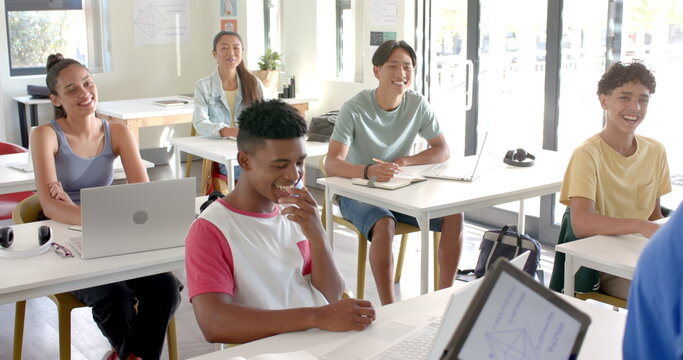 In high school, teenagers using laptops and smiling in classroom, enjoying lesson
