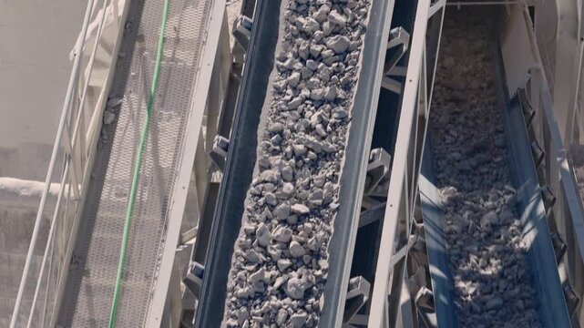 Slow motion aerial of parallel conveyor belts carrying gravel in sunlight