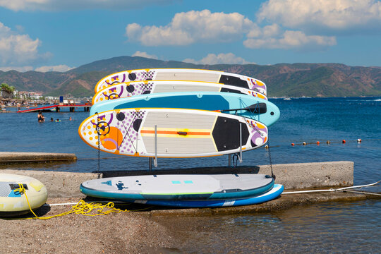 Colorful standup paddleboards (SUP) arranged on a rental rack at a beach resort, ready for rent. Conceptual photo representing water sports equipment rental, active summer holiday, and sea activities.