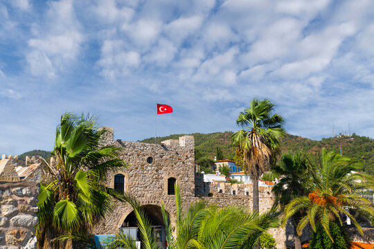 Closeup view of Historic Marmaris castle with Turkish flag and tropical palm trees under blue sky, Mugla, Turkey