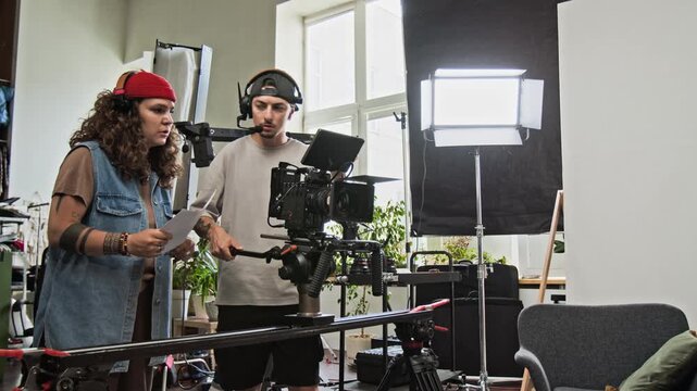 Young adult Caucasian director discussing scene composition with camera operator on studio set. Clip perfect for video production marketing, creative tutorials, and backstage media projects