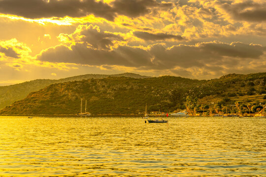 Dramatic golden sunset clouds with light rays over Sogut village coast and boats, Marmaris, Turkey
