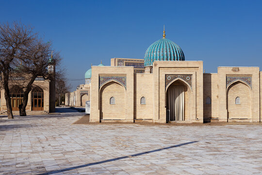 Muyi Muborak Madrasah in Tashkent with turquoise dome and ornate arches on a clear winter day. Historic Islamic building facade with empty stone plaza, ideal for travel and cultural publications.