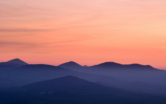 Layered blue mountain silhouettes under a soft pink and orange twilight sky