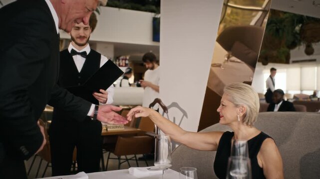 Senior Caucasian couple walking to dining table guided by young adult waiter and receiving menu card. Clip suitable for luxury hospitality advertising, fine dining promotions, and lifestyle projects