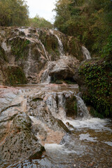 Scenic small waterfall cascading over rocky tufa formation in green forest © Laura