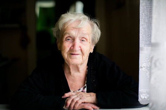 Portrait of an elderly woman resting her folded hands by a window and looking slightly away in soft natural light