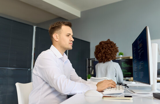 Developer programmer man coding at computer in office. Focused software engineer writes clean code at desktop monitor in a modern workplace. Ideal for business technology teamwork and output.