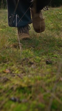 Vertical shot of traveler legs in boots walking slowly along grass trail in nature. Perfect for outdoor recreation campaigns, hiking equipment ads, ecotourism promotions