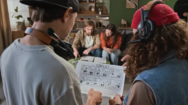Young adult film crew members discussing storyboard with Caucasian actors on movie set. Suitable for promoting filmmaking courses, creative agency teamwork, or media production workflows
