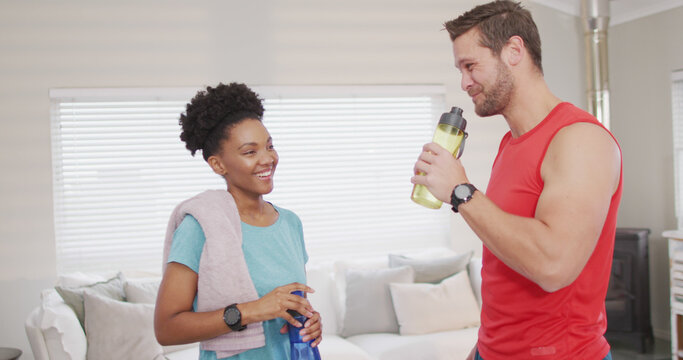 Image of happy diverse couple drinking water after training at home