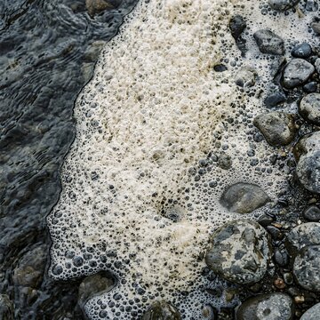 Close up of sea foam bubbles on pebbles by the water.