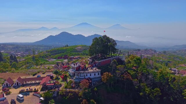 Aerial view of a hilltop viewpoint building with layered mountain ranges and blue sky. Drone footage of Central Java highlands, tourism, and scenery.
