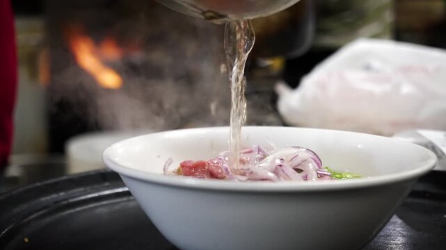 Hot steaming broth pours into a bowl of traditional Vietnamese pho with beef Dramatic lighting and steam close up slow motion 4K