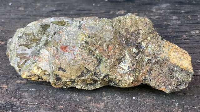 Gold Ore Nugget: A raw, unpolished nugget of gold ore, displaying metallic luster and crystalline structures, resting on a textured wooden surface.