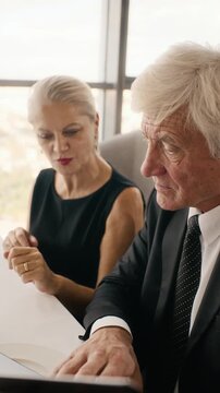Vertical video of senior Caucasian couple reading restaurant menu and discussing food choices at table. Clip suitable for luxury hospitality marketing and retirement lifestyle campaigns