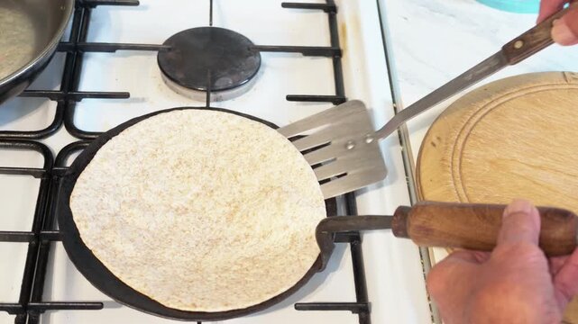 Roti flatbread pressed with a slotted spoon on a hot tava during cooking