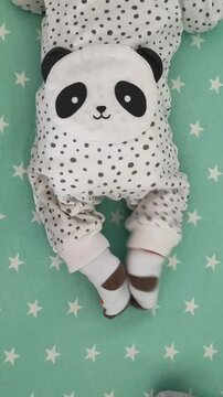 Baby in white polka dot onesie with panda face appliqu&eacute; lying on green star patterned sheet, top down vertical view.