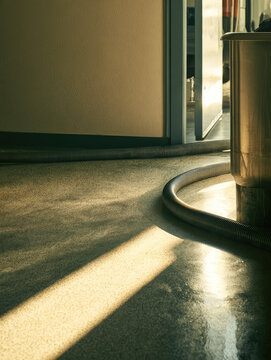 Grease suction hose beside stainless tank on polished terrazzo floor with warm morning sunlight and industrial cleaning service atmosphere