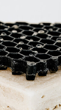 Black trickling filter media with water droplets on travertine pedestal creates minimalist environmental technology study with crisp geometric texture and open space