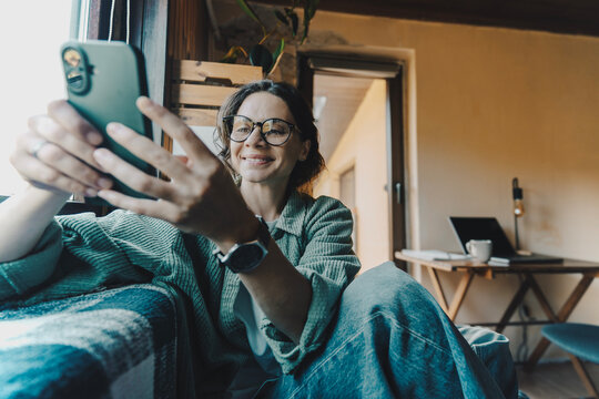 Young woman in green shirt and glasses looking at phone in countryside home office