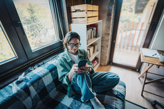 Young woman in green shirt and glasses looking at phone in countryside home office