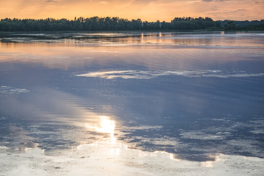 The surface of a lake reflecting the sky, clouds, and the sun in the evening, shortly before sunset&mdash;a minimalist landscape suitable as a background