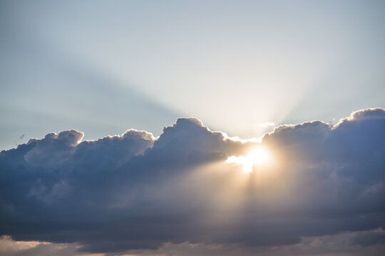 Sunbeams shining through clouds high in the sky during the evening, just before sunset&mdash;a warm, atmospheric landscape for a background