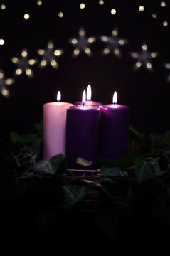 Cozy Advent arrangement: Lit purple and pink candles in a natural wreath, Christmas time.