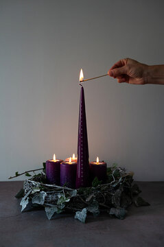 Hand lighting tall purple Advent candle, the traditional Christmas preparation.