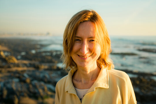 Close up portrait of a smiling woman on a rocky seashore in warm golden evening light