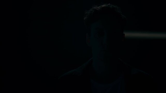Portrait of young adult Caucasian man looking at camera while light ray scanning across face in darkness. Ideal for cybersecurity, biometric identity verification or mental wellbeing storytelling