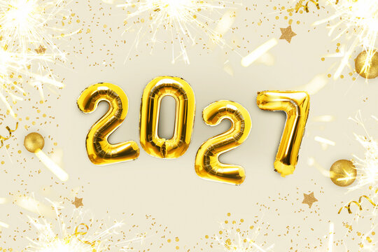 Happy New Year 2027 concept with golden foil number balloons, bright sparkling sparklers, confetti, and golden ornaments on light background. Festive holiday party banner design.