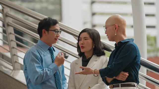 Three professionals converse near a modern railing. Man gestures while speaking. The woman listens attentively
