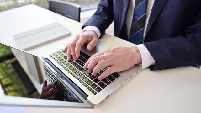 A close-up video of the hands&mdash;with no face visible&mdash;of a male businessman in a suit typing on a computer keyboard in a clean, well-maintained office, Enter into AI