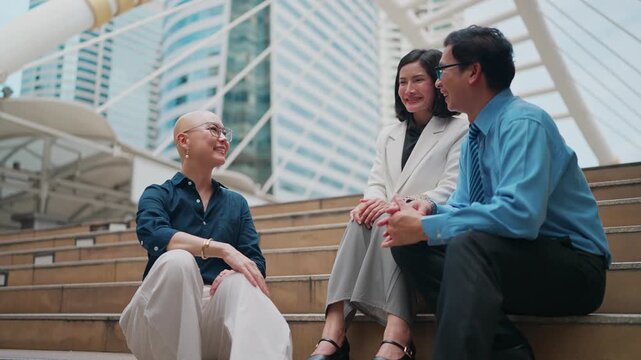 Three colleagues laugh while seated on city steps. They gesture joyfully, sharing a moment of genuine connection