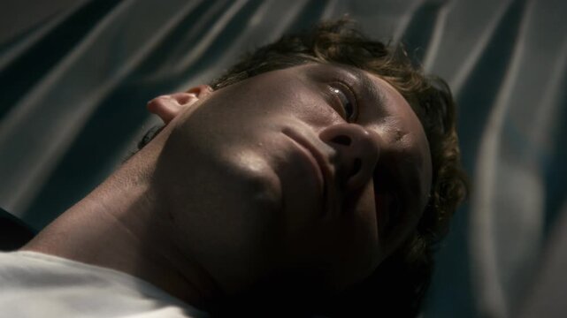 Caucasian young adult man lying down, opening eyes with shocked expression in extreme close up. Footage suitable for medical emergency, trauma recovery, or sleep disorder awareness campaigns