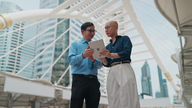 Two professionals review data on a tablet outdoors. They stand beneath a modern architectural structure
