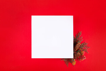 Blank Christmas holiday white card for greetings or invites, on festive bright red background with fir tree branches, top view copy space © ricka_kinamoto