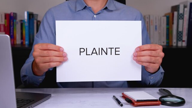 Une personne en chemise tenant une feuille de papier sur laquelle est &eacute;crit en gros le mot plainte.