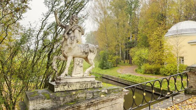 Pan shot sweeps past a classical centaur statue on a bridge in slow motion. Golden autumn trees evoke a majestic and serene mood. Shot in Pavlovsk Park, Russia.