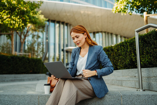 Businesswoman working remotely on a laptop outdoors at a modern office