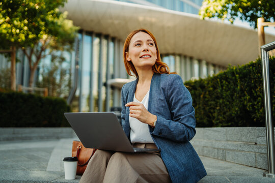 Businesswoman working on a laptop outdoors in a modern urban setting