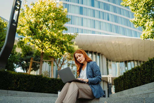 Businesswoman working remotely on a laptop outside a modern office building