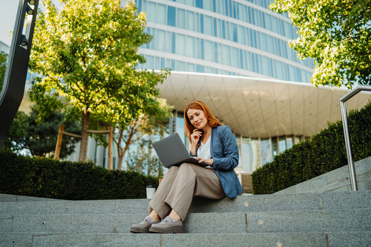 Businesswoman working on a laptop outside a modern office building