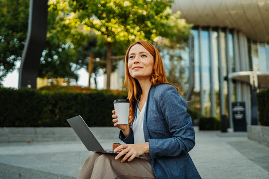 Businesswoman working remotely with laptop and coffee in a city plaza