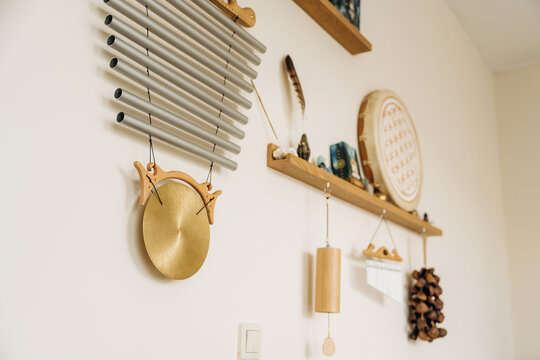 Metallic wind chime with circular gong and wooden hanging decorations on a softly lit cream wall in a cozy interior arrangement