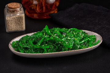 Glass jar of white seeds, dark cloth napkin and white ceramic oval plate with green seaweed chuka salad © Andrei Starostin