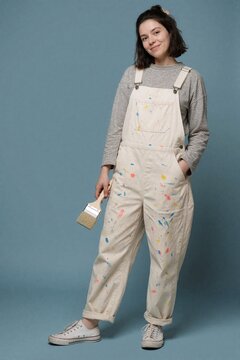Young woman in paint-splattered overalls holding a brush