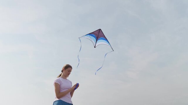 Smiling girl flying a kite with long ribbon tails against a cloudy sky slow motion view from below